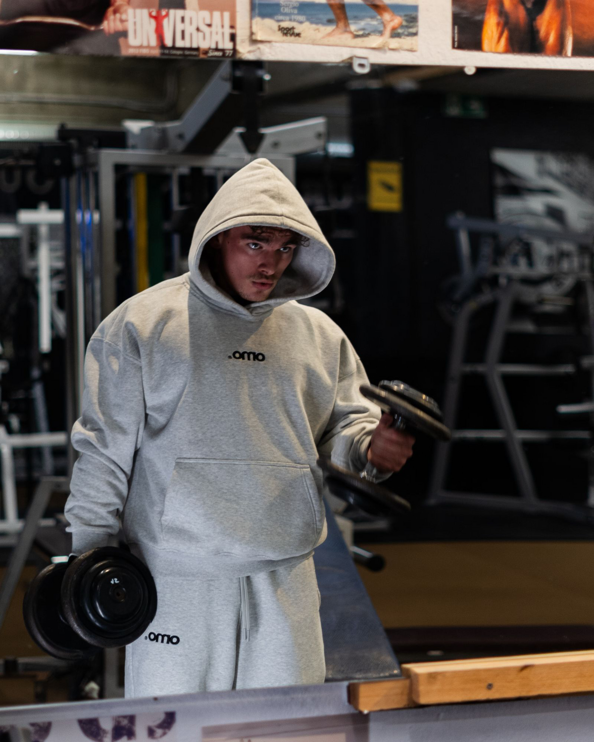 Model trägt omo Essential Hoodie und Essential Jogger in Grau beim Training im Gym